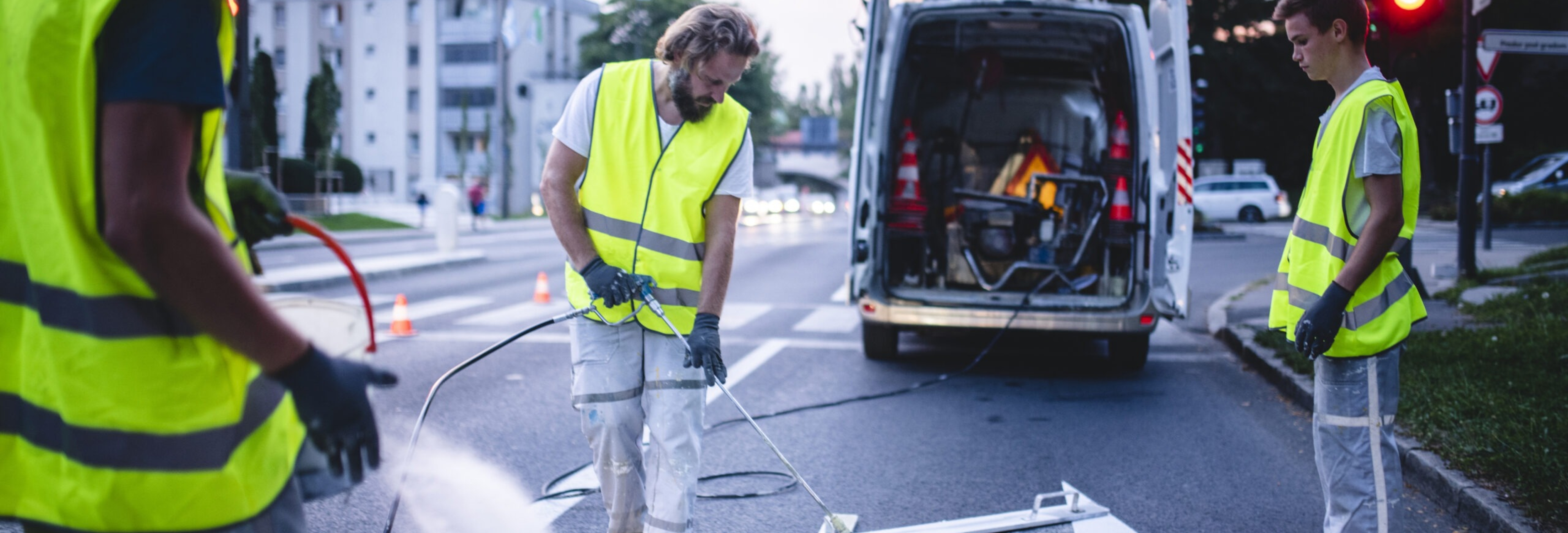 Three-man construction crew in reflective vests spray painting turn arrow marking in Central European capital city.