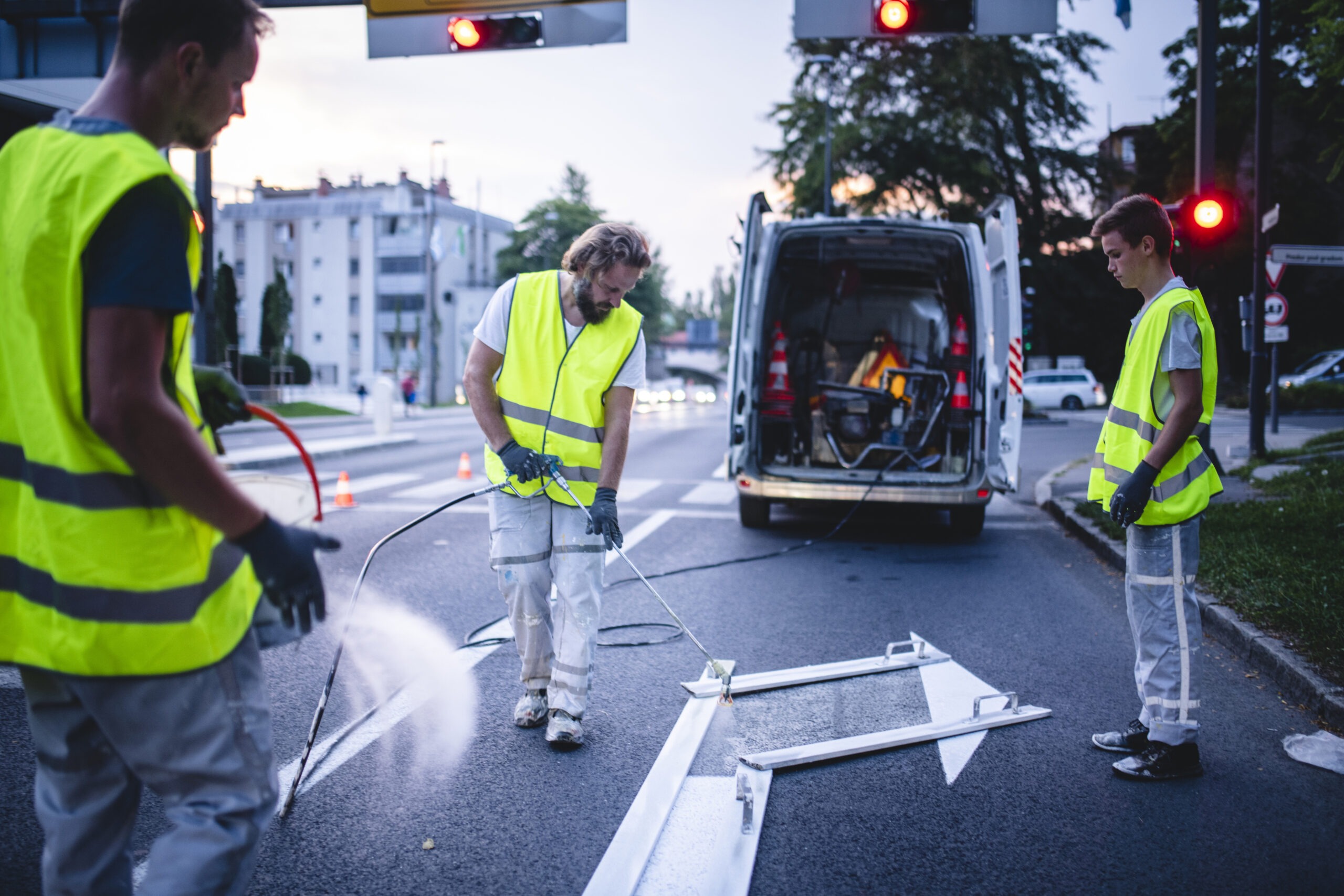 Three-man construction crew in reflective vests spray painting turn arrow marking in Central European capital city.